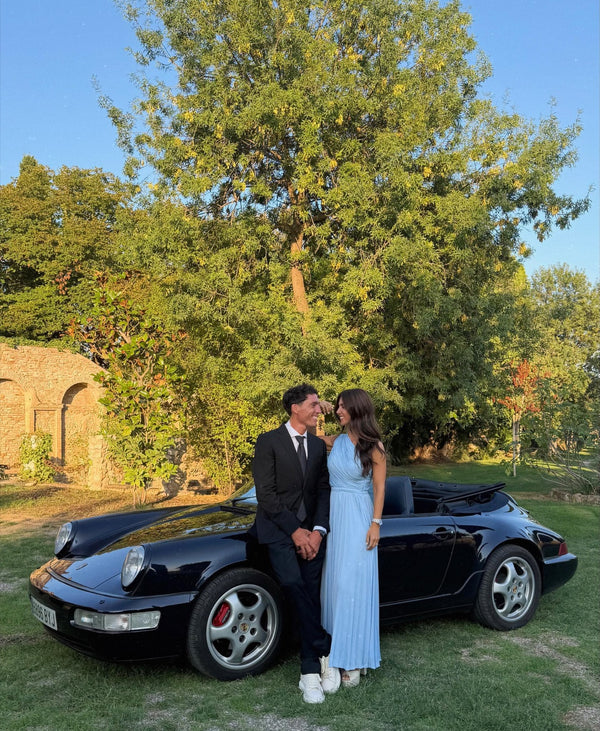 Couple in formal wear beside a black Porsche 911 in a garden